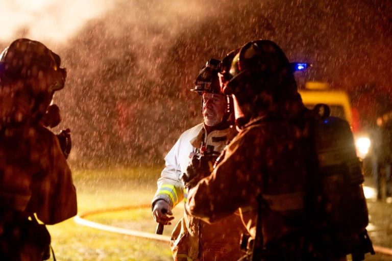 Group of firefighters talking at night with water droplets falling around them
