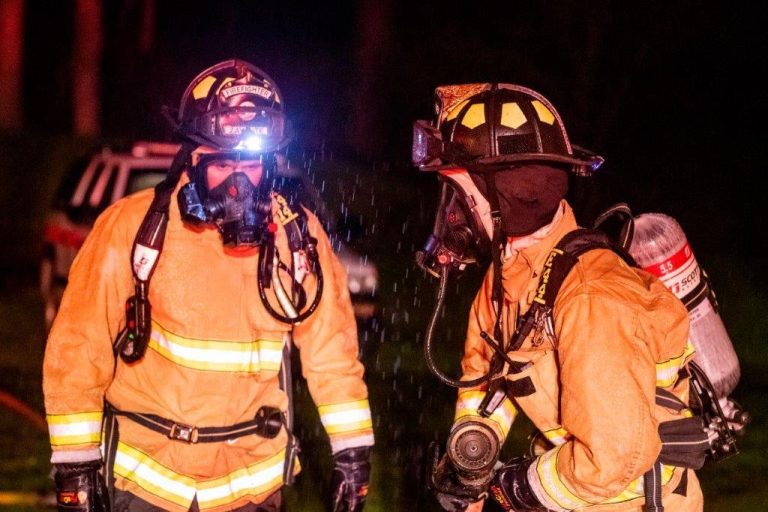 Two firefighters looking at each other with water mist falling from the sky at night