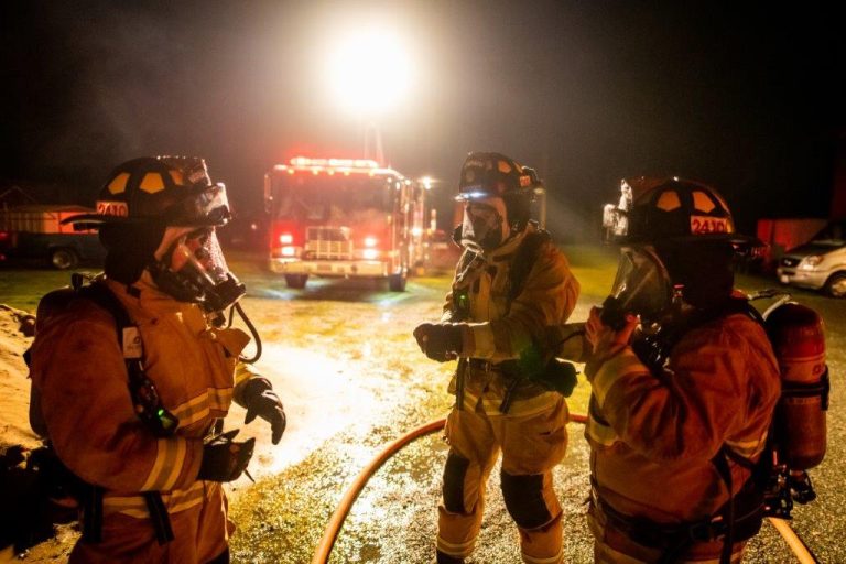 Three firefighters standing in front of a truck at night