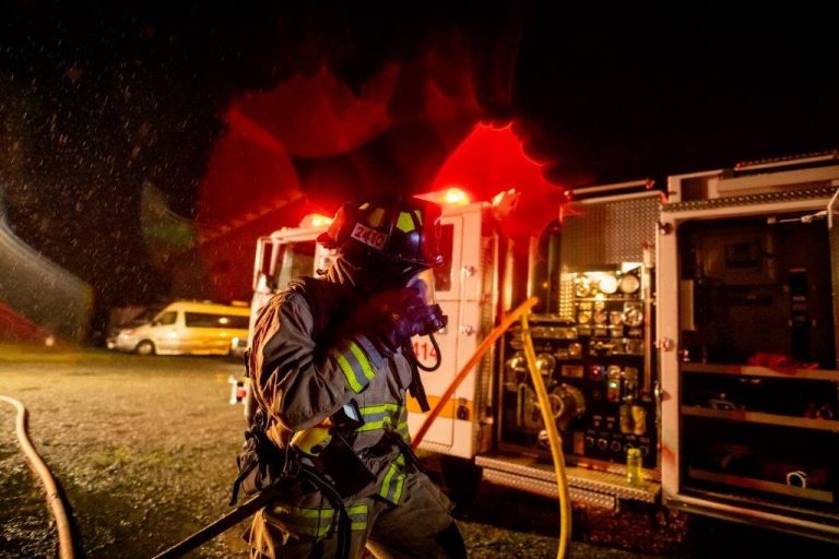 Firefighter at night near truck with hoses